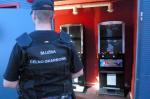 Funkcjonariusz KAS przed wejściem do lokalu, w którym widać maszyny do gier hazardowych