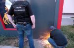 Funkcjonariusz KAS wycina zawiasy w drzwiach piłą do metalu