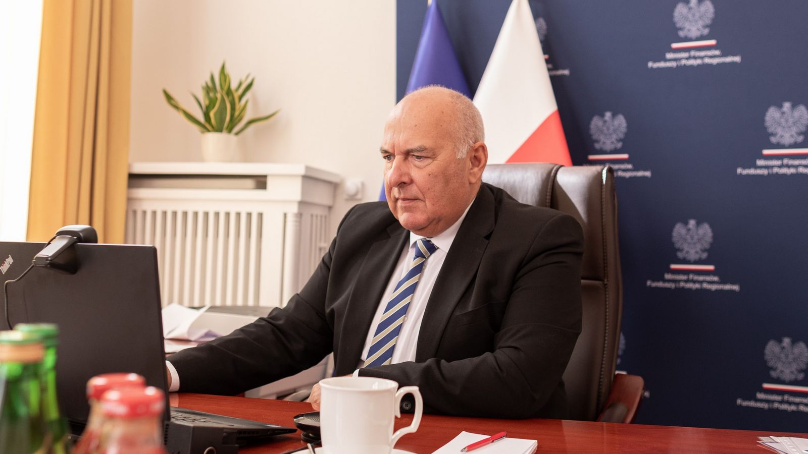 Minister Tadeusz Kościński siedzi w swoim gabinecie. Przed sobą ma otwarty laptop.