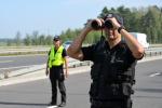 Funkcjonariusze Służby Celno-Skarbowej podczas kontroli stoją na drodze, jeden patrzy przez lornetkę.