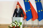 Szef KAS przemawia przy mikrofonie, w tle flagi Polski i Unii Europejskiej