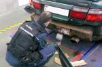 Funkcjonariusz KAS wyjmuje papierosy ukryte pod zderzakiem samochodu
