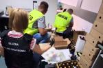 Funkcjonariuszka KAS i dwóch policjantów przy kartonach z zatrzymanym alkoholem